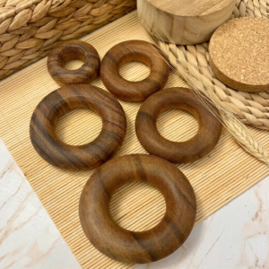 Anillas de madera en tonos marrones oscuros repartidas sobre una esterilla de bambú, junto a una base de corcho.