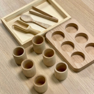 Set de trasvases de madera con los utensilios dentro de la bandeja y los cubiletes sobre una mesa de madera.