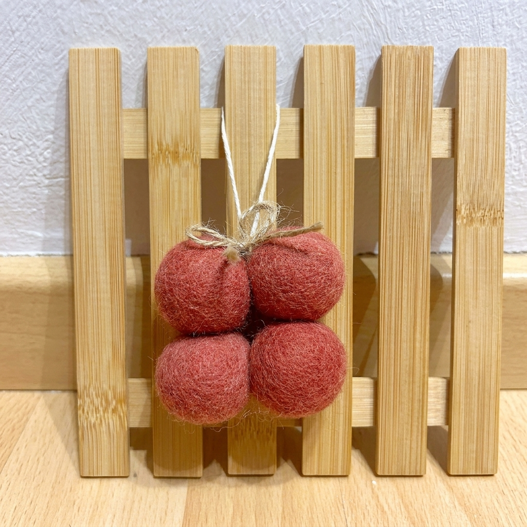 Minicolgante de cuatro bolas de fieltro de lana en color rosa, colgado sobre un panel de bambú.