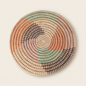 Decoración de pared multicolor de fibra natural: tapete redondo de hierba kaisa trenzada en espiral, con puntadas de algodón blanco crudo, naranja, lila, azul claro y azul oscuro, sobre fondo crema.